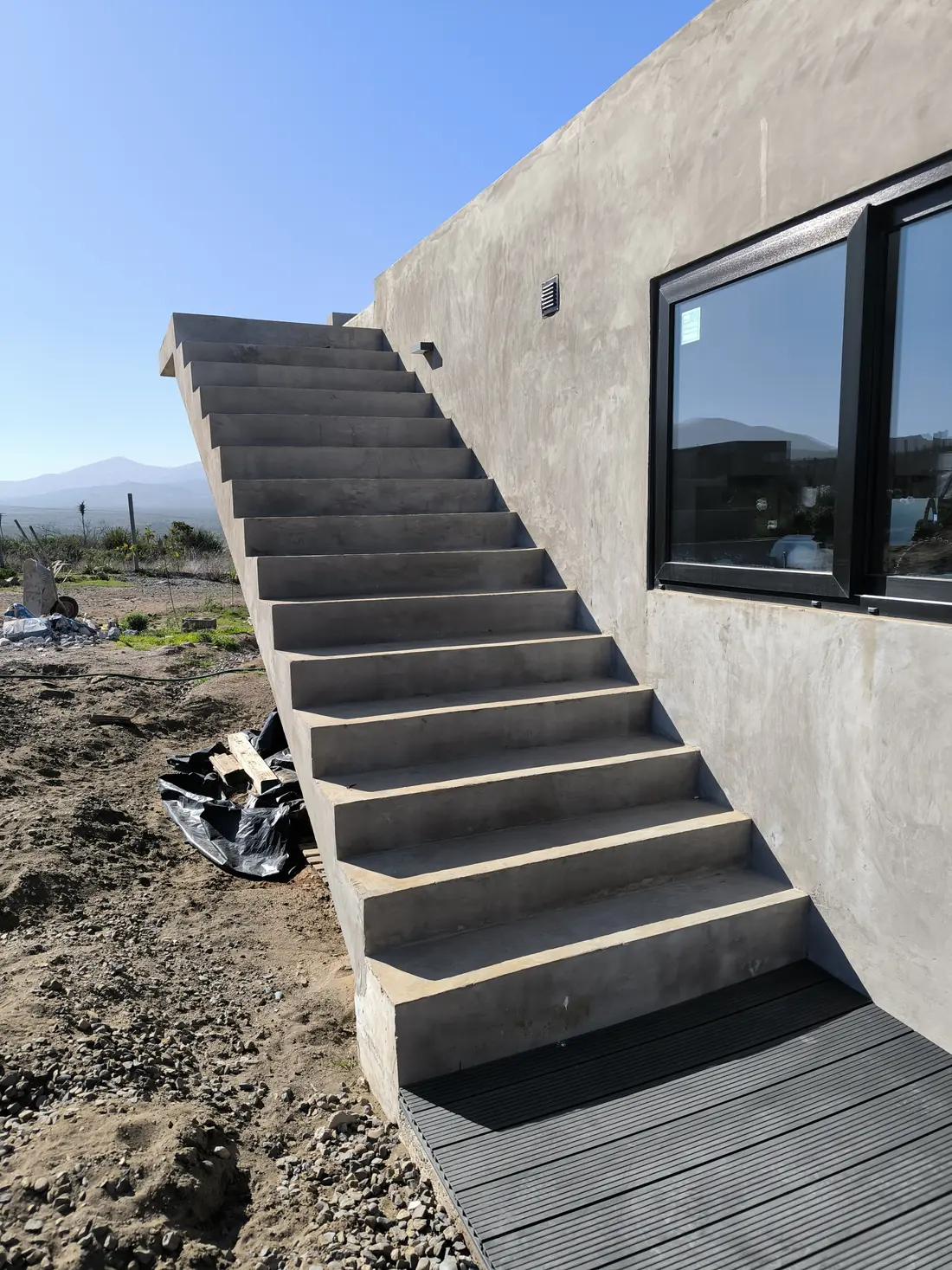 Escalera exterior de hormigón en voladizo contra el muro, con el valle y los cerros al fondo