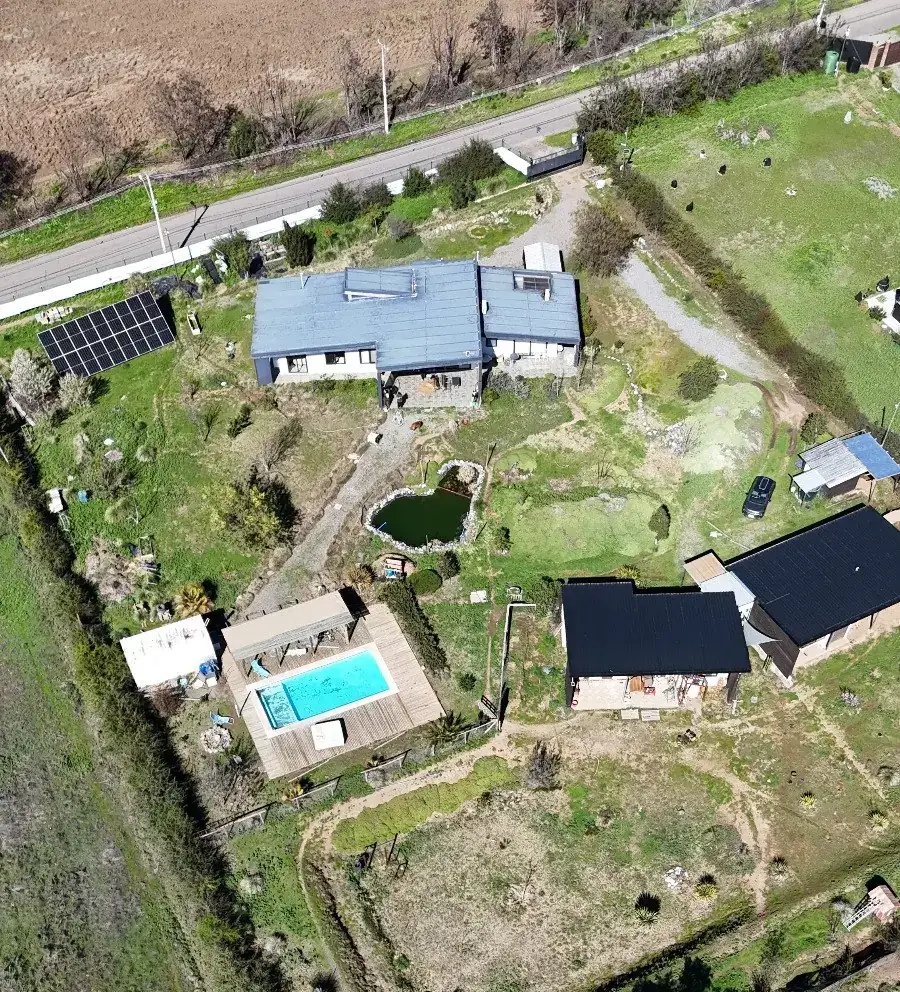 Vista aérea oblicua: vivienda principal con paneles solares, laguna, piscina y el volumen del quincho