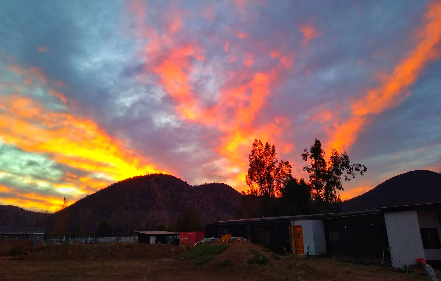 Atardecer sobre la parcela con los cerros al fondo y las casas terminadas a la derecha