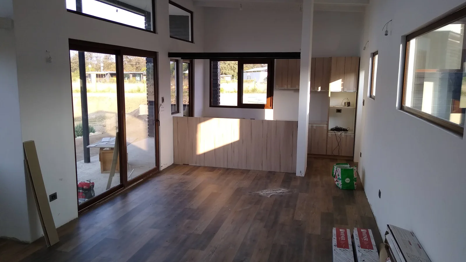 Estar terminado con piso de madera, ventanas altas y cocina abierta con mesón de madera clara