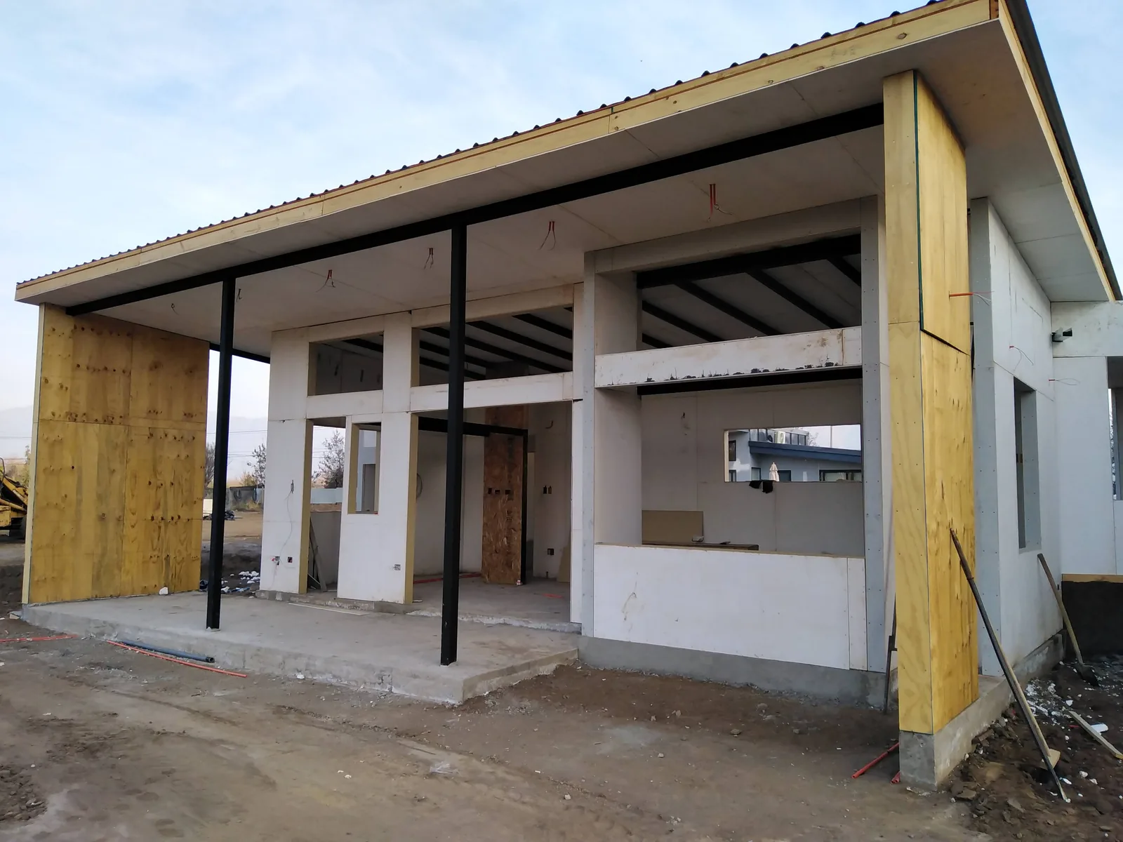 Obra gruesa: pilares de acero negros, vigas y paneles cerrando la fachada bajo el alero