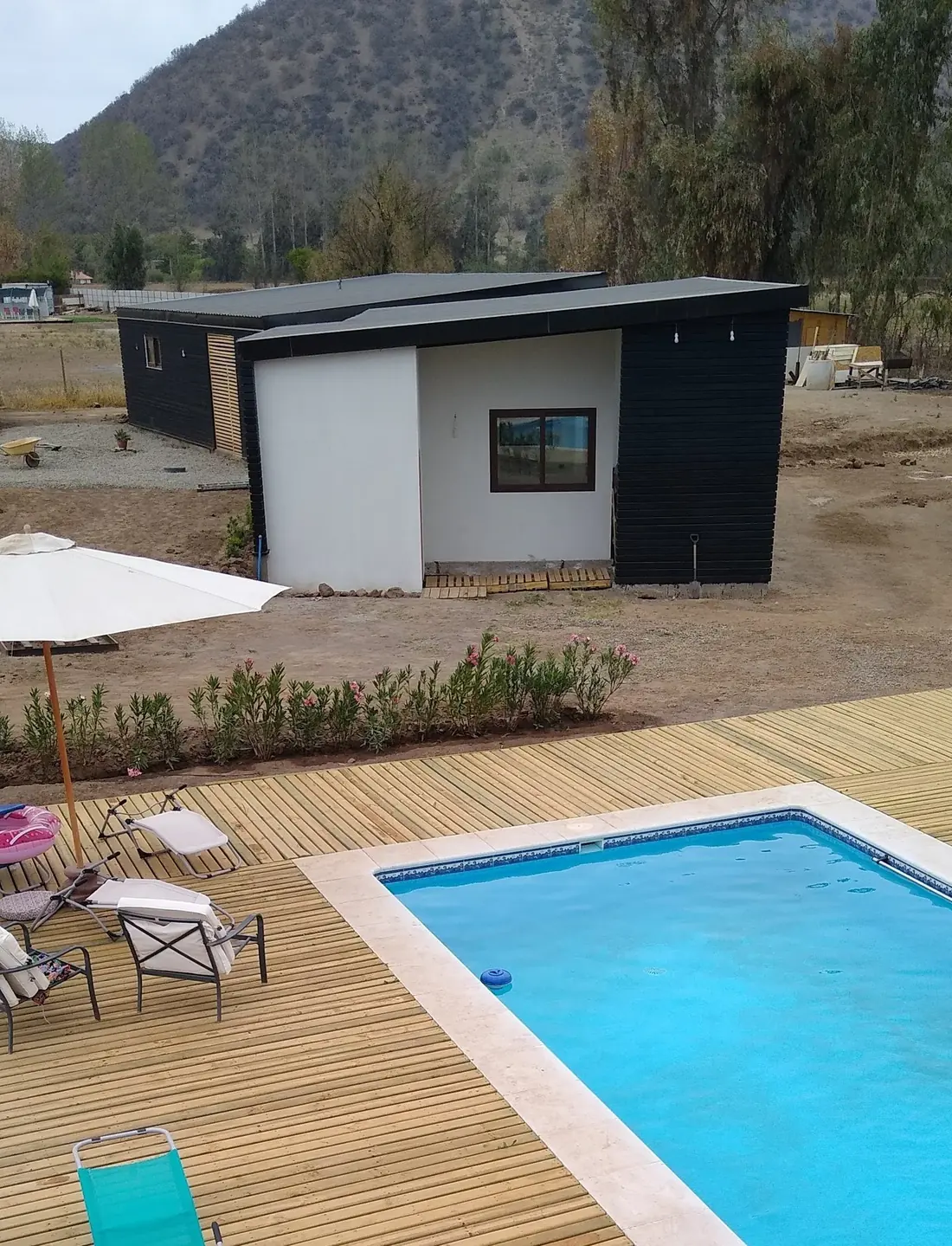 Piscina con deck de madera y, al fondo, volumen de bodega y quincho con revestimiento negro