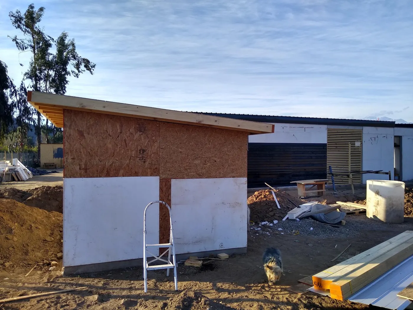 Volumen en construcción con paneles OSB y placas, junto a la casa ya revestida en negro
