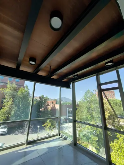 Oficina en Ciudad Empresarial: esquina vidriada con cielo de madera y vigas metálicas negras