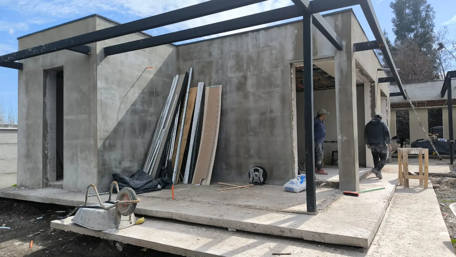Casa VJ en Pirque en obra: los volúmenes de hormigón estucado, la estructura de acero del alero y la terraza, con la cuadrilla trabajando